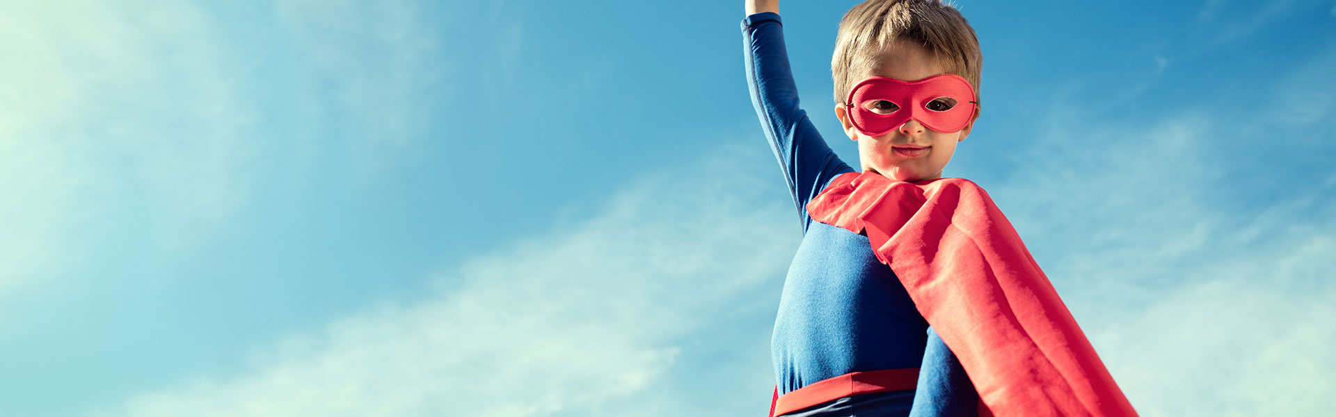Child wearing superhero costume in front of a blue sky
