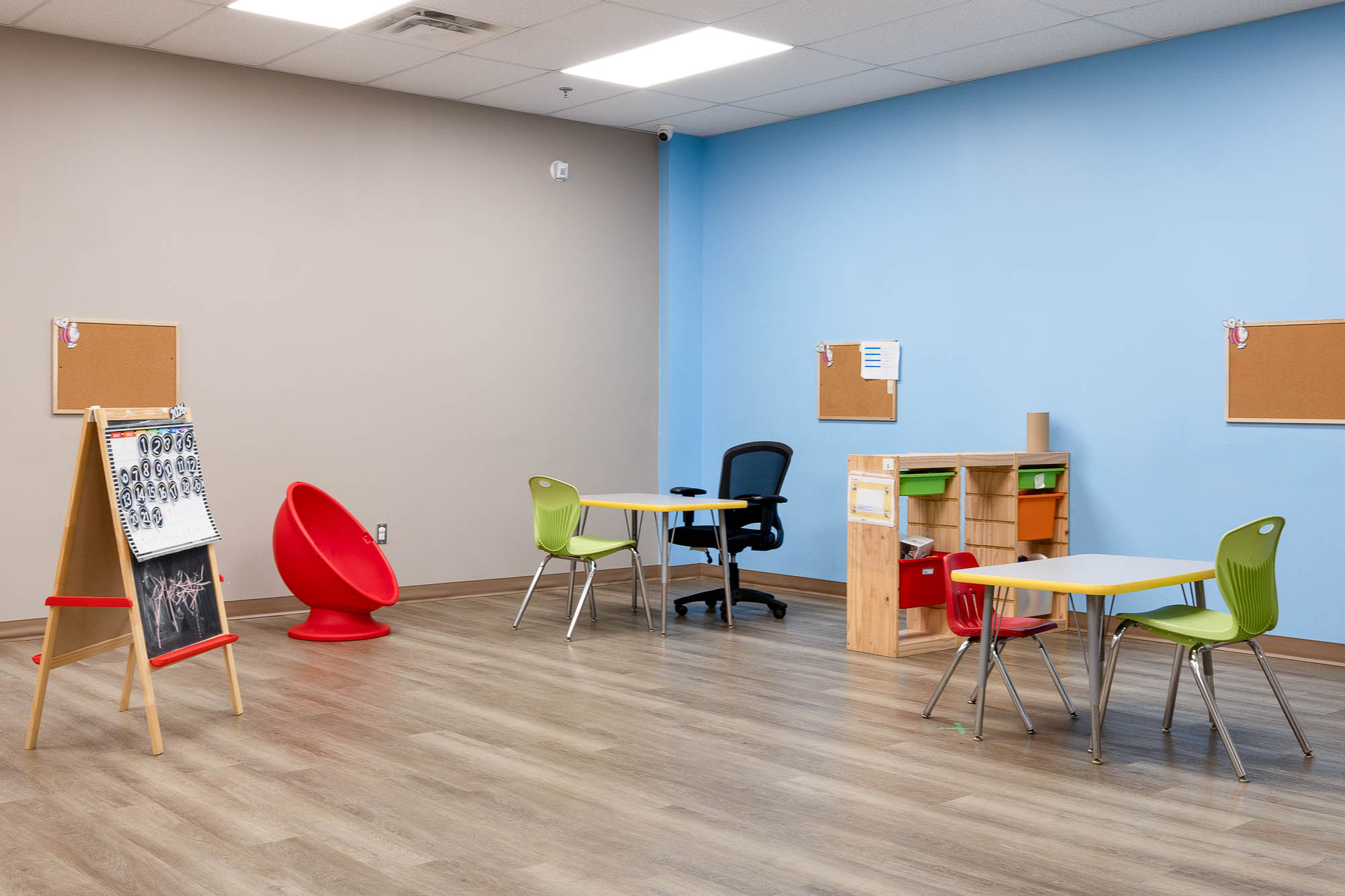 Bright therapy room at AlphaBee Etobicoke with an easel, small tables and a red chair